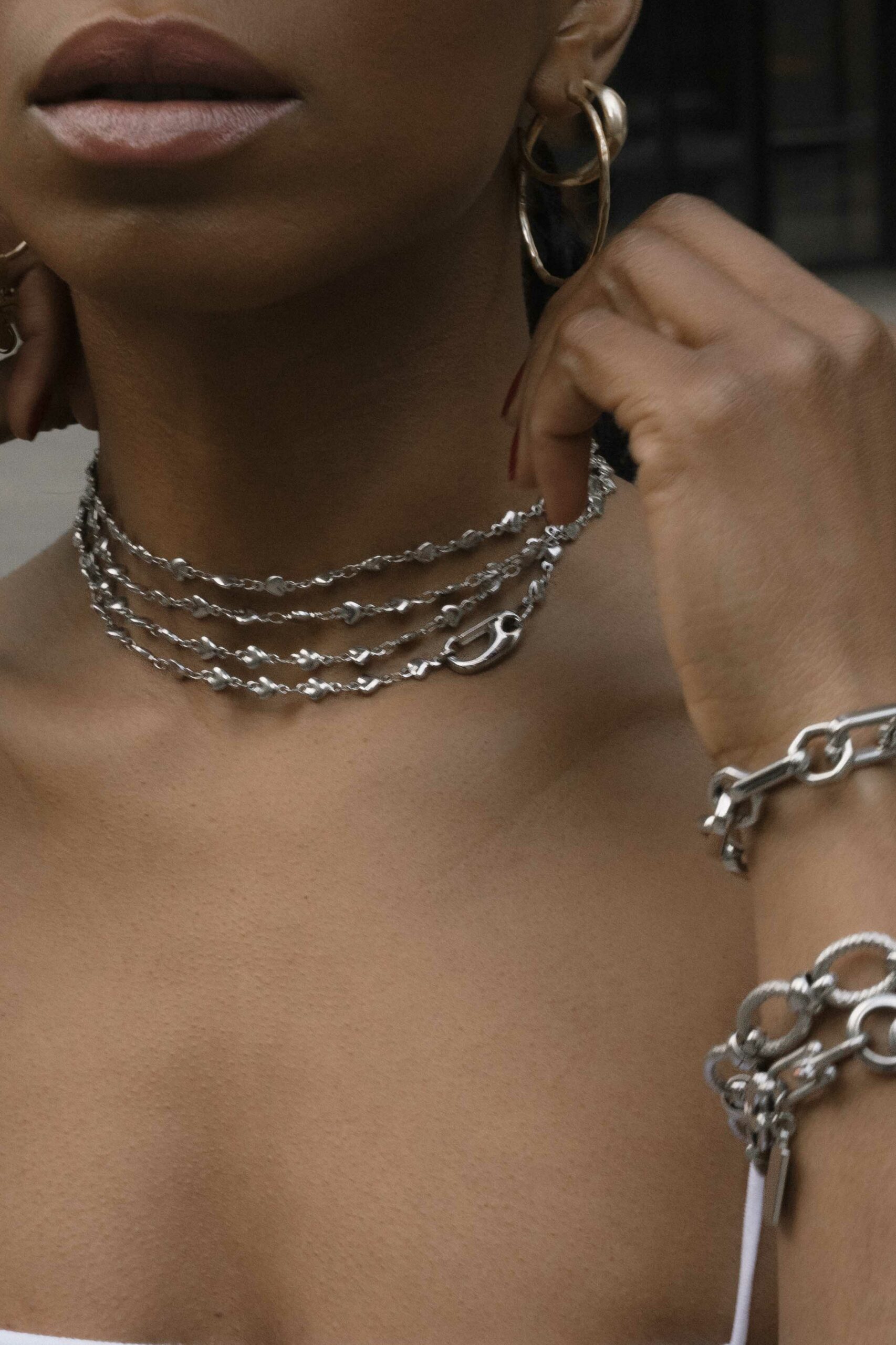 A detail photo of a woman in a white tennis dress adjusting her silver necklaces